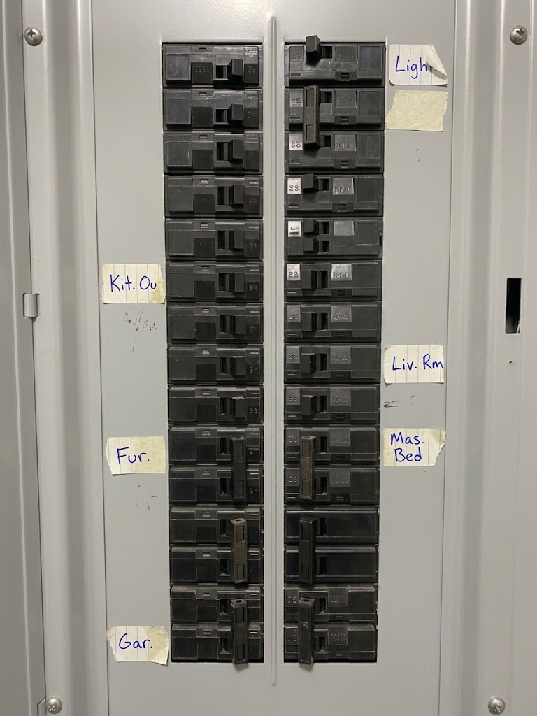 A panel deadfront filled with breakers and torn, illegible masking tape labels